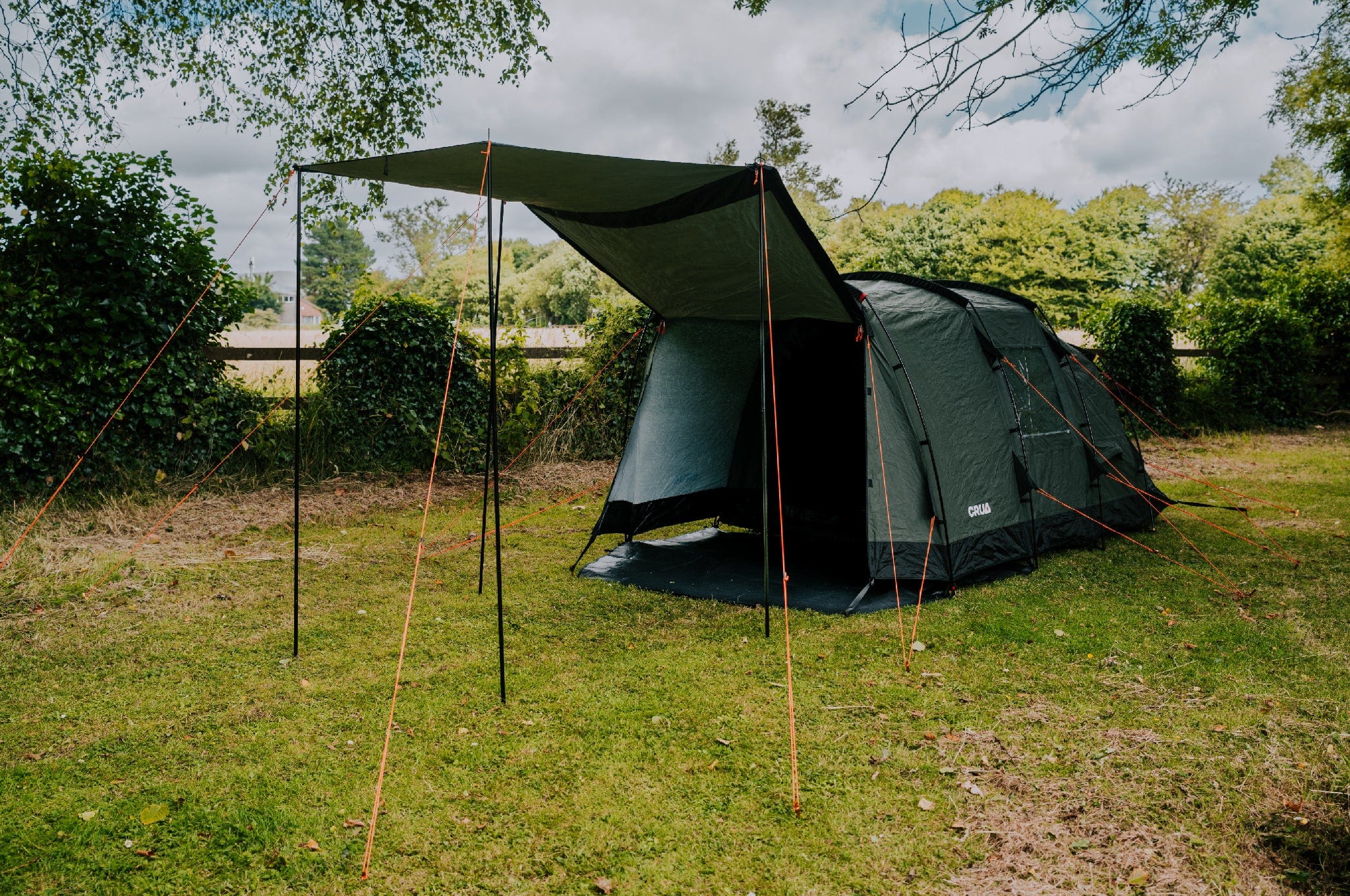 Crua Tri camping tent set up on grass with trees, awning fully extended, ideal for outdoor adventures.