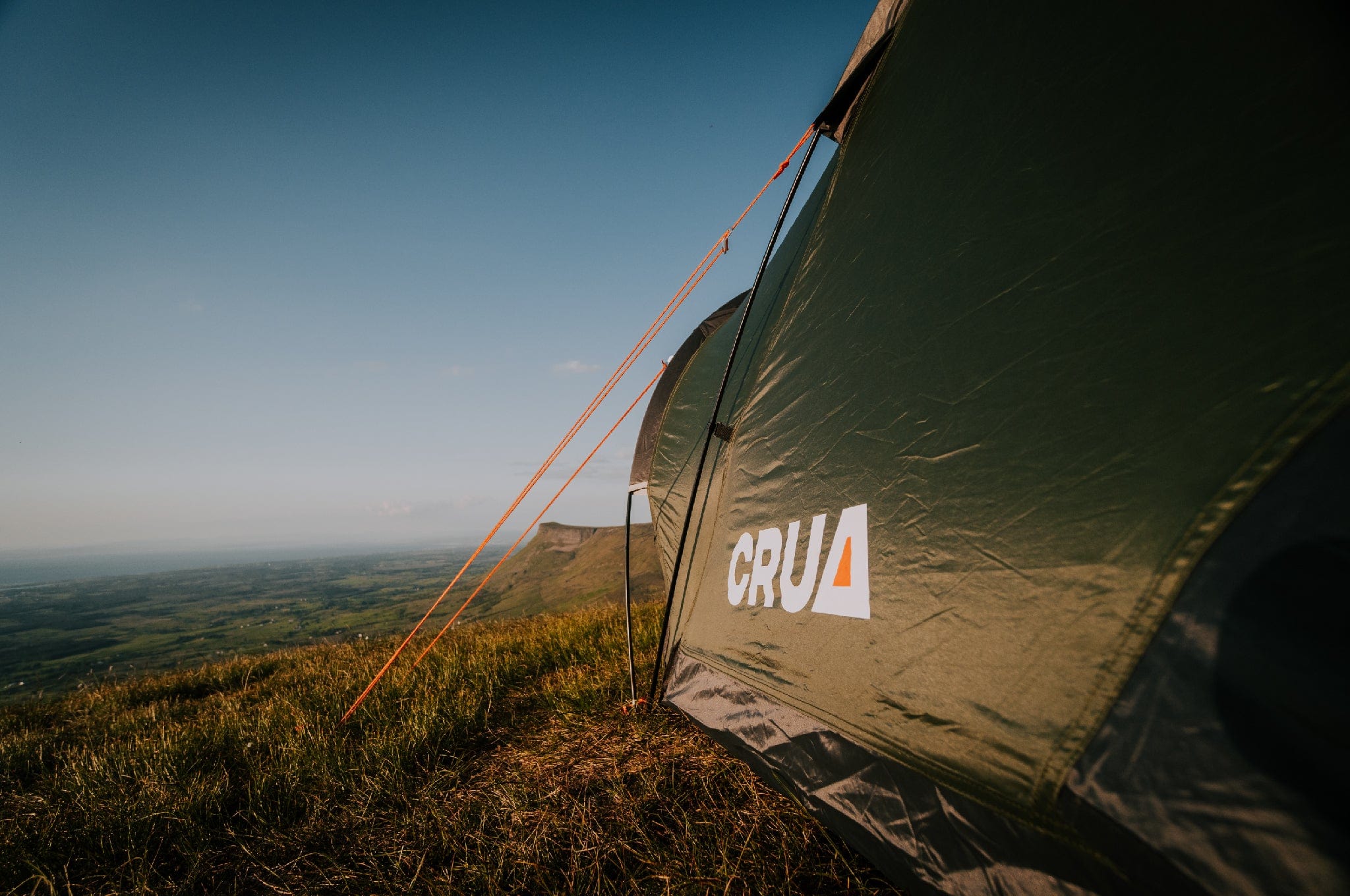 "Side view of the Duo GS Maxx with Crua logo, pitched on a hill overlooking a scenic valley, emphasizing outdoor adventure."